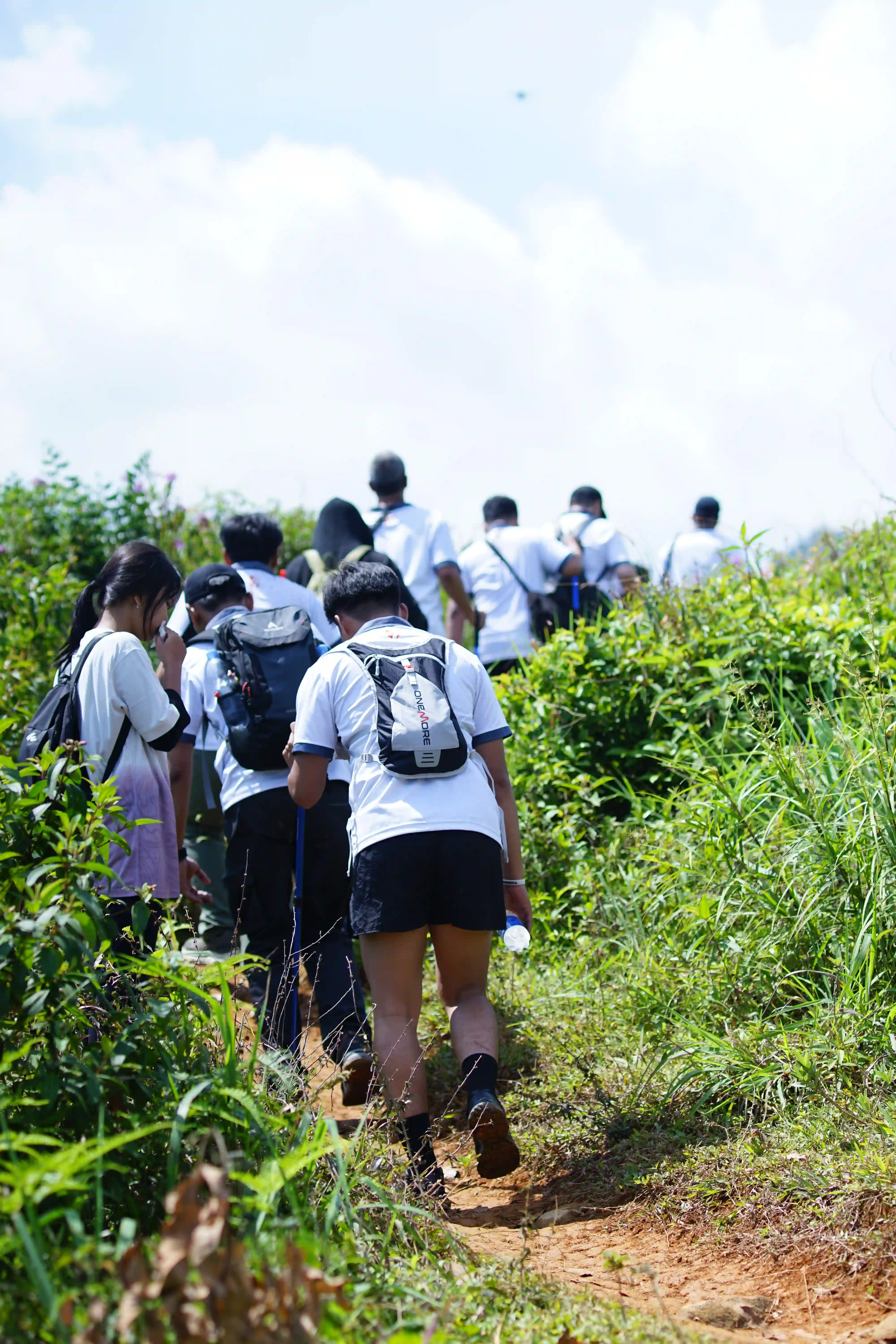Sekelompok peserta trekking berjalan di area terbuka dengan latar perbukitan hijau.