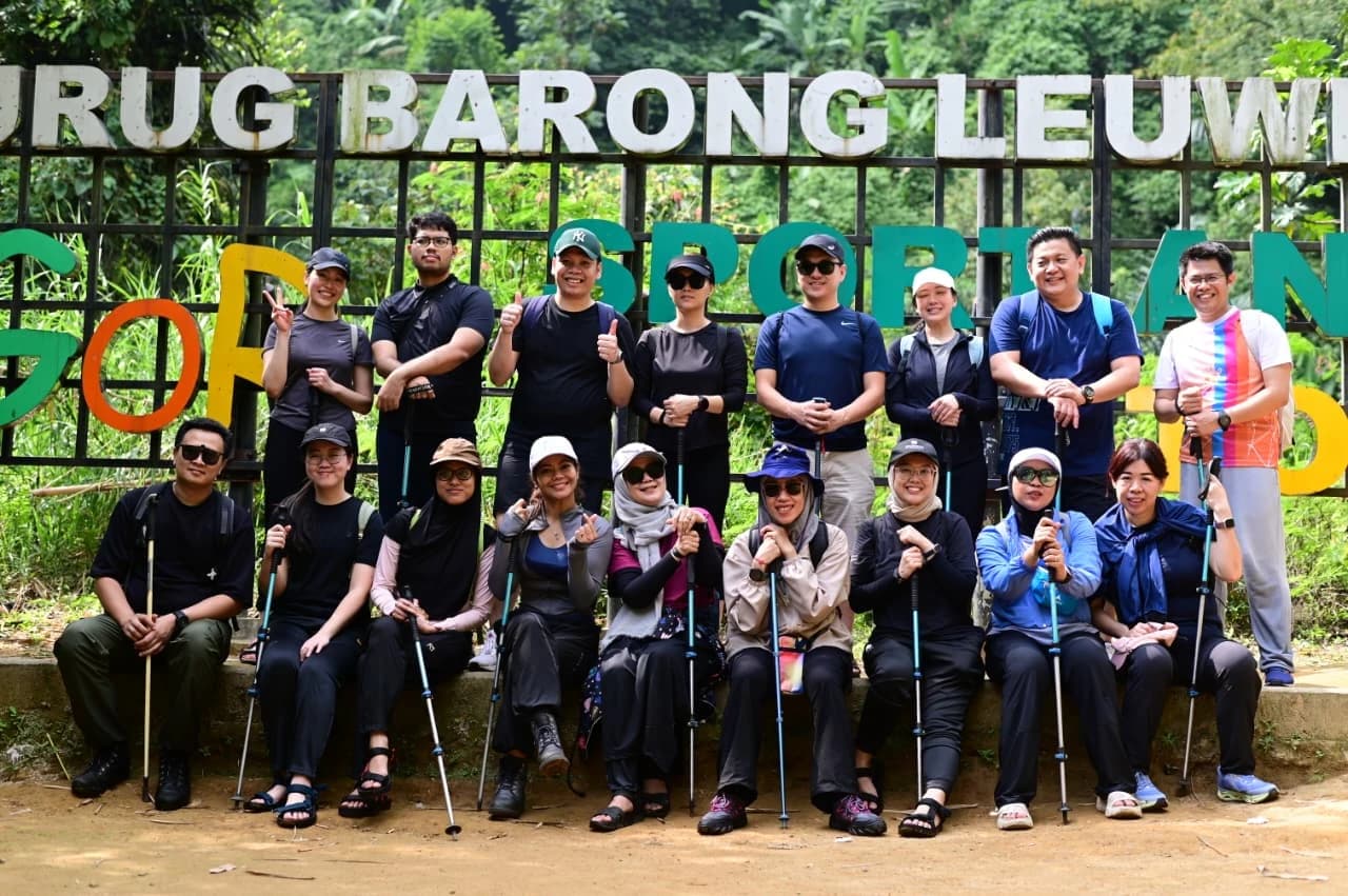 Rombongan peserta yang ceria berjalan di jalur tanah yang lebar dengan latar pepohonan rimbun.