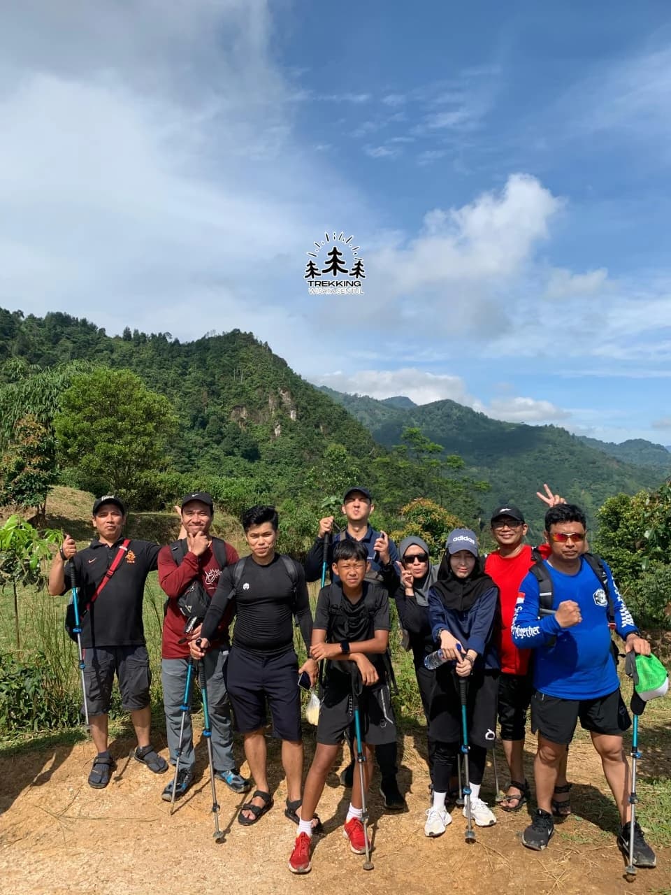 Peserta melintasi jembatan bambu sederhana di atas aliran sungai yang berbatu.