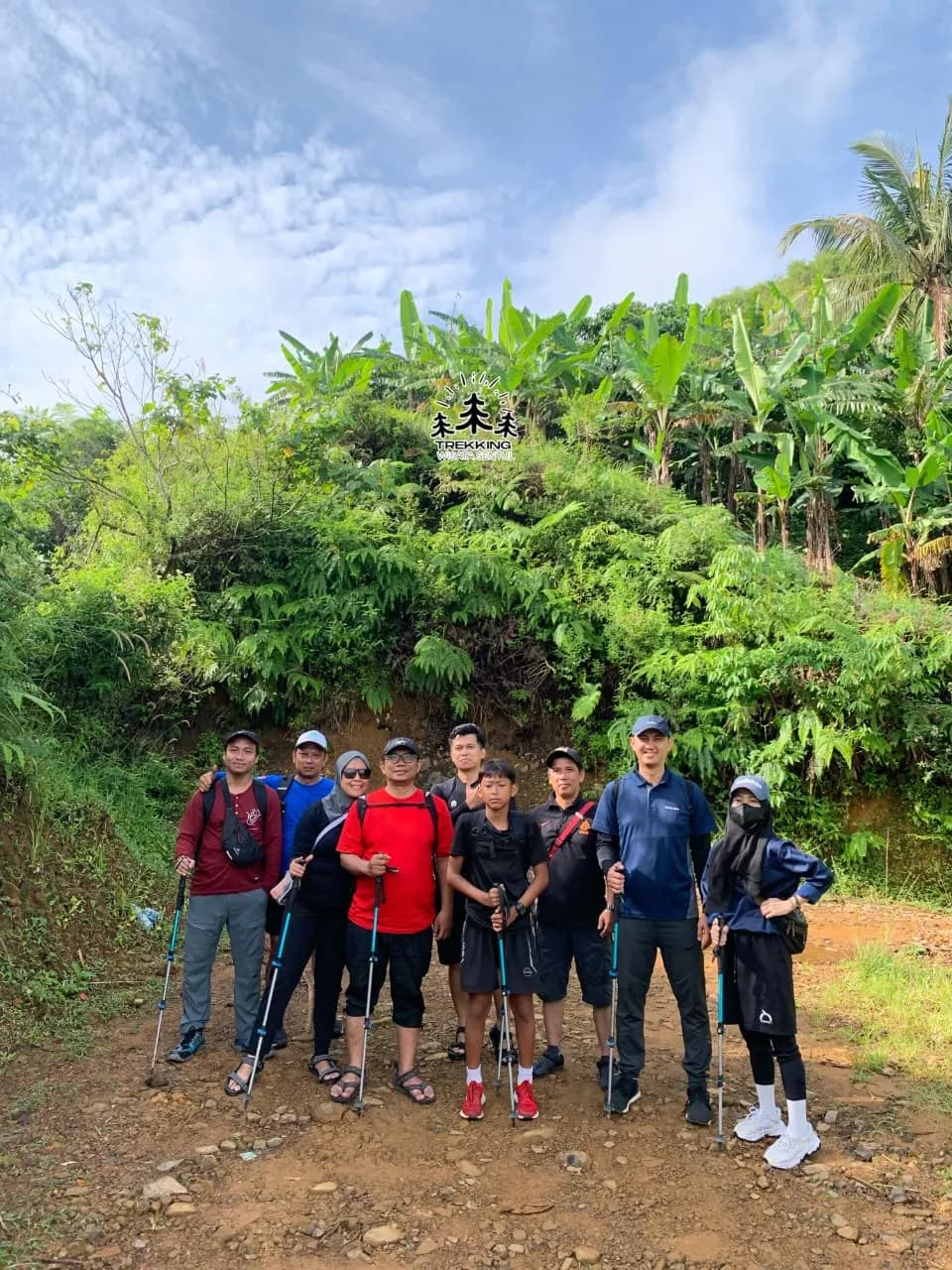 Sekelompok peserta berfoto bersama di jalur setapak dengan latar belakang pepohonan hijau.