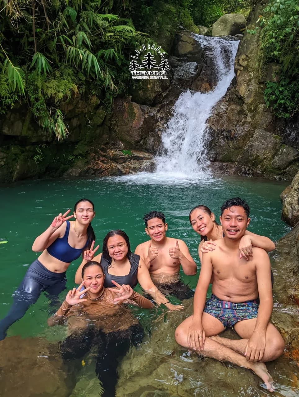 Foto grup outing perusahaan dengan spanduk di padang rumput berlatar gunung.