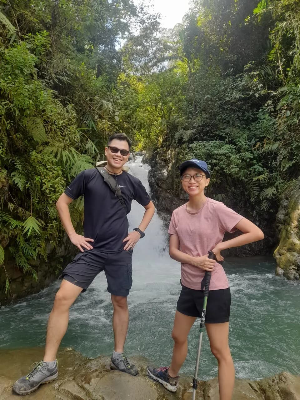 Sepasang peserta berpose di depan curug yang indah di tengah hutan.