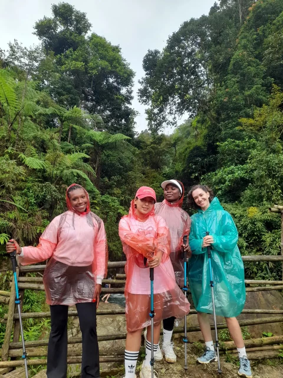 Empat peserta wanita ceria menggunakan jas hujan warna-warni saat trekking.