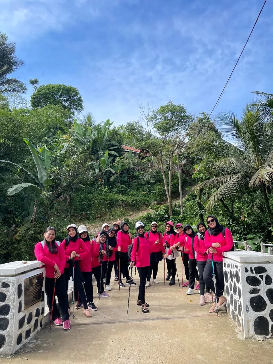 Seorang peserta berhijab berpose di depan Curug Kencana yang dikelilingi pepohonan.