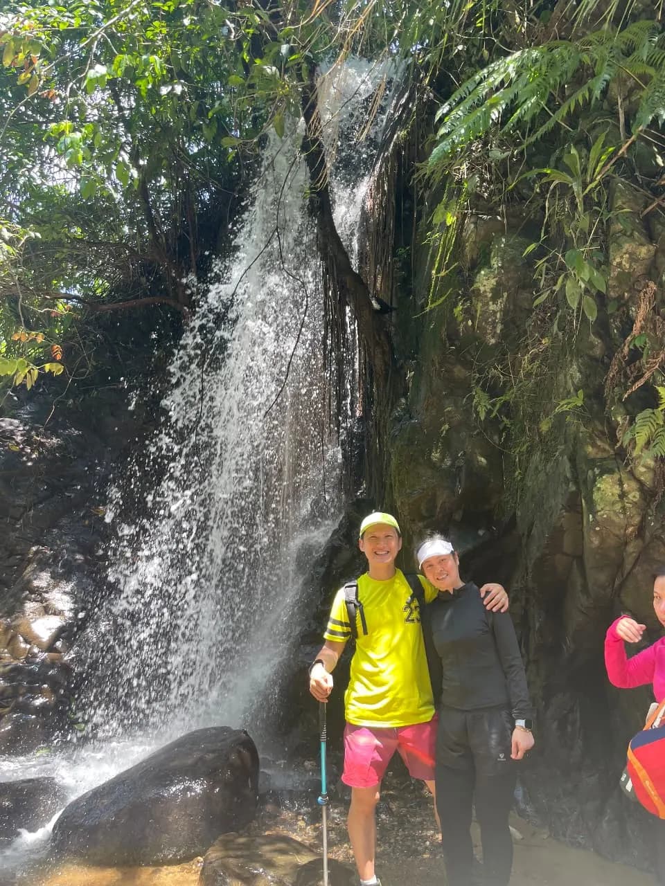 Seorang pendaki wanita menikmati pemandangan perbukitan hijau dari titik pandang.
