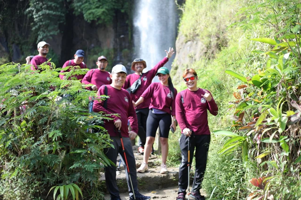 Beberapa peserta berjalan di jalur setapak di antara pepohonan hijau menuju curug.