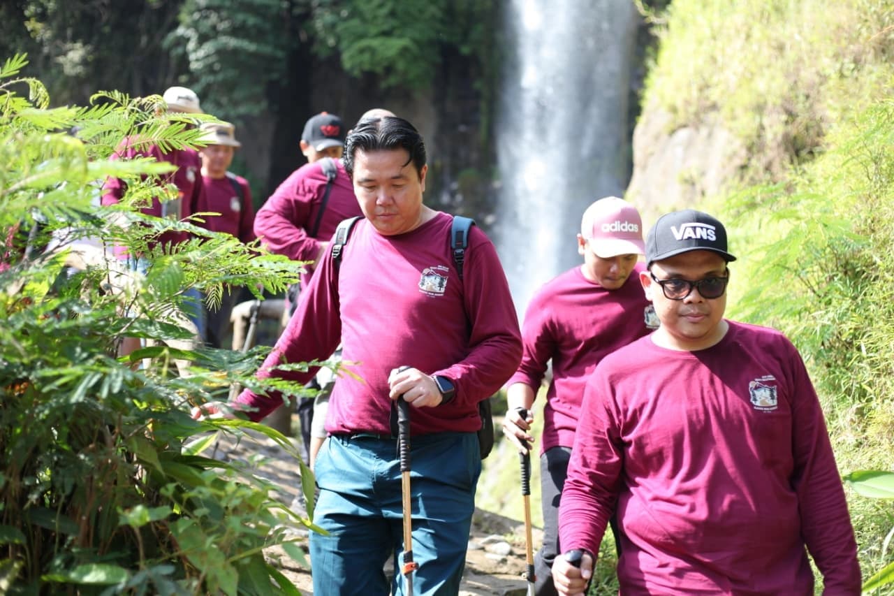 Foto grup besar di depan sebuah curug dan papan nama.