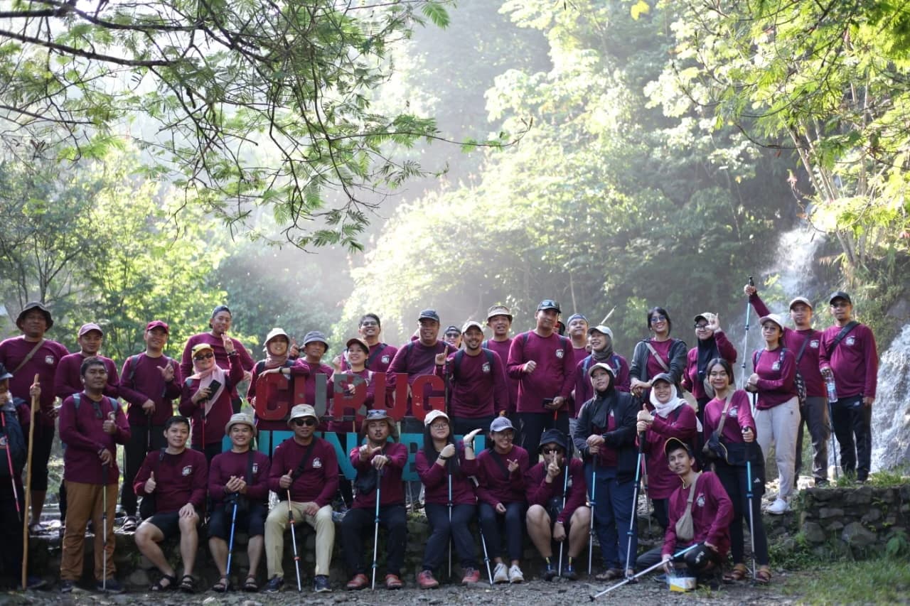 Seorang peserta pria berpose di jembatan batu dengan pemandangan air terjun.